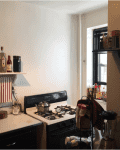 Small kitchen with gas stove, shelves with spices, utensils, and a blender near a window.