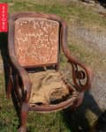 Worn-out wooden armchair with torn upholstery and intricate backrest design on grass.