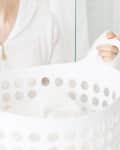 Person in a white robe holding a white laundry basket with clothes.