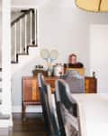 Staircase with plaid carpet, wooden sideboard with vintage decor, and dining chairs in a bright room.