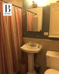 Small bathroom with pedestal sink, striped shower curtain, and wall-mounted cabinet.