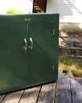 Green metal cabinet with double doors and silver handles on a wooden table outdoors, labeled "Before" in red.