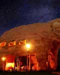 Elephant-shaped straw building illuminated by torches under a starry night sky.