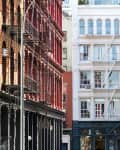 Historic New York City street with red, white, and beige buildings featuring fire escapes and arched windows.