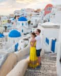Couple embracing on a cobblestone path in Santorini, with white buildings and blue domes in the background.