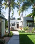 Pathway leading to a white house with green awnings, surrounded by palm trees and a well-maintained garden.