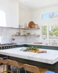 Bright kitchen with marble countertops, green cabinets, open shelves, and a large island with wicker stools.