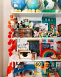 Children's bookshelf with globes, stuffed animals, educational books, wooden toys, and colorful decor.