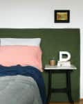 Bed with green headboard, pink pillow, and blue blanket next to a small table with books, a plant, and a letter "D" decor.