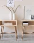 Two wooden side tables with books, vases, and framed art against a beige wall.