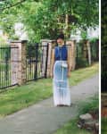 Woman in a sheer white skirt, left in denim top by a fence, right in a long-sleeve blouse against greenery.
