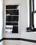 Hanging black and white organizer with scissors and towel in a tiled bathroom corner.