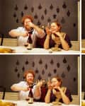 Couple at a dining table opening wine, laughing, and enjoying drinks against a decorative wall.