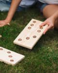 Person playing giant wooden dominoes on grass.