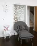 Gray lounge chair with patterned pillow, white side table with red branches, and floral frosted glass door.