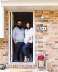 Couple standing in doorway of brick house with house number 3501, potted flowers, and outdoor light fixture.