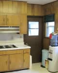Wood-paneled kitchen with electric stove, oven, and water cooler next to a door and window.
