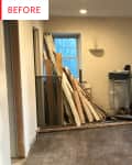 Empty room with wood planks stacked against the wall, a window, and a dust collector on a worn wooden floor.