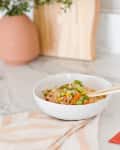 Bowl of vegetable fried rice with chopsticks on a marble countertop, next to a red chopstick wrapper and a striped cloth.