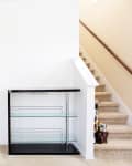 Empty living room corner with a glass shelf unit beside carpeted stairs.
