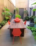 Outdoor patio with a wooden table, red chairs, and potted plants along brick walls.