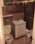 Small bathroom with pink tiles, white sink, toilet, mirrored cabinet, and a bathtub with a glass door.