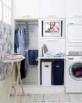 Laundry room with floral wallpaper, stacked washer and dryer, ironing board, and clothes hanging on a rack.