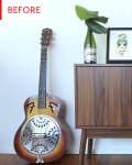 Mid-century modern cabinet with a framed artwork, potted plant, wine bottle, and resonator guitar leaning against it.