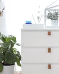 White dresser with leather handles, potted plant, and small glass terrarium on top.