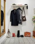 Entryway with patterned tile floor, coats on hooks, boots, red shoes, a lantern, and a brown leather bag.