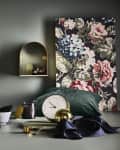 Decorative setup with a glowing bulb, floral canvas, gold accents, green pillow, and a white cup on a green surface.