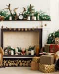 Cozy living room with a decorated fireplace, antlers, gifts, and a chair draped with a plaid blanket.