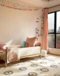 Cozy children's room with a small sofa, colorful bunting, and a large window overlooking trees.