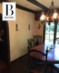 Dining room with wooden table, black spindle chairs, rustic chandelier, and arched brick doorway.