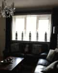 Dimly lit living room with black leather sofa, chandelier, and decorative bottles on window sill.