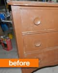 Worn brown wooden dresser with three drawers and large round knobs in a cluttered garage.