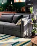 Gray sectional sofa in a modern living room with green accents, plants, and a striped rug.