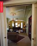 Living room with green walls, ornate ceiling, chandelier, piano, armchair, and red rug.
