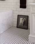 Bathroom with white subway tiles, black and white patterned floor, framed portrait, and white cabinet.