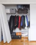 Open closet with hanging jackets, storage boxes, and suitcases on wooden floor.