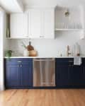 Modern kitchen with navy lower cabinets, white upper cabinets, stainless steel dishwasher, and wooden floor.