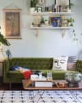 a living room with a green velvet sofa, accent pillows, greenery, and shelves with decor