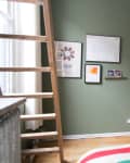 Loft bedroom with green walls, ladder, framed art, and a black shelf holding decor items and a folded blanket.
