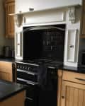 Traditional kitchen with wooden cabinets, black countertops, and a large black stove with a white decorative hood.