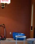 Living room with brown walls, vacuum cleaner, blue bag, and small white table with books.