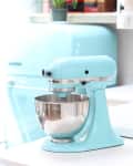 Aqua blue stand mixer on a white countertop with a stainless steel bowl.