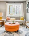 Living room with gray sofa, colorful pillows, orange ottoman, and stained glass windows.