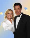 A man in a tuxedo and a woman in a white blouse smiling, with a colorful cloud and heart background.