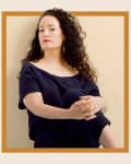 Person with curly hair in a navy outfit sitting against a beige background, framed by a brown border with text "Lora Appleton 2020."