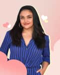 Woman in a blue striped blazer with hoop earrings, standing against a pink background with heart graphics.